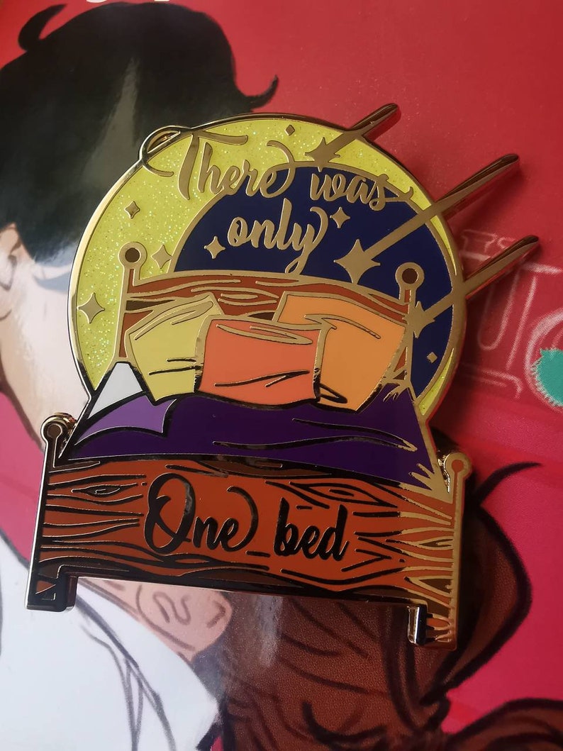 Puede incluir: Pin de esmalte dorado con un lecho con almohadas y un cielo estrellado. El texto "There was only one bed" est&aacute; escrito en la cama.