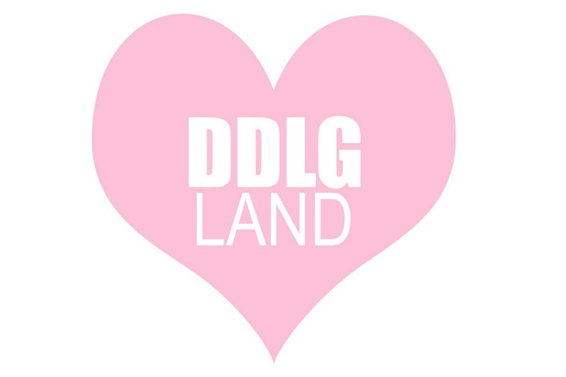 K&ouml;nnte beinhalten: Ein rosa Herz mit dem wei&szlig;en Schriftzug "DDLG LAND". Das Herz hat eine einfarbige, pastellrosa Farbe, und der Text ist zentriert innerhalb der Herzform.