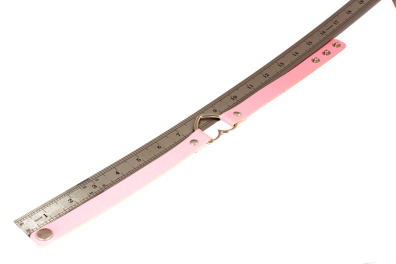 K&ouml;nnte beinhalten: Ein hellrosa Choker-Halsband mit herzf&ouml;rmiger Mitte und silberfarbener Hardware. Ein Metalllineal liegt zur Messung neben dem Halsband. Das Halsband ist etwa 48 cm lang.