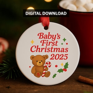 May include: A white ceramic Christmas ornament with the text "Baby's First Christmas 2025" in red. A brown teddy bear holds a candy cane. The ornament has a red ribbon for hanging.