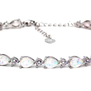 以下が含まれることがあります： 梨型の白いオパールと小さな透明なキュービックジルコニアの石が並んだシルバーブレスレットです。