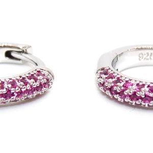 Può includere: Un paio di orecchini a cerchio in argento con un design di pietre rosa. Gli orecchini sono contrassegnati "925" sul retro.