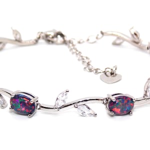 Puede incluir: Una pulsera de plata con un diseño de vid que presenta ópalos negros y piedras de circonita cúbica transparentes.