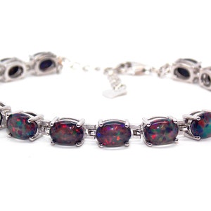Puede incluir: Un brazalete de plata con cierre de cadena y piedras de ópalo negro de forma ovalada.
