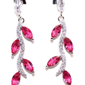 May include: A pair of silver-coloured drop earrings. Each earring has a marquise-cut clear stone at the top, a curved stem of small clear stones, and several fuchsia-coloured leaf-shaped stones. The earrings are set against a white background.