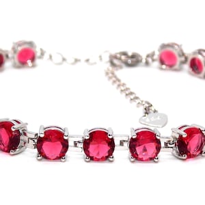 May include: A silver bracelet featuring a row of round, red gemstones. The bracelet has a heart-shaped charm.