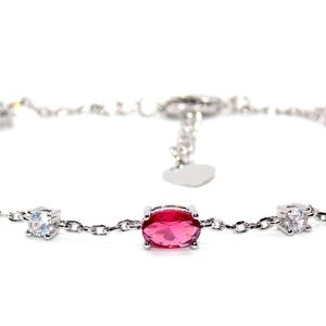 May include: A silver bracelet with oval and square-cut red gemstones and clear accent stones. The bracelet has a delicate chain and a heart-shaped charm near the clasp. The jewellery is displayed against a white background.