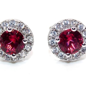 Könnte beinhalten: Ein Paar silberne Ohrringe mit einem roten Edelstein, der von einem Heiligenschein aus kleineren weißen Edelsteinen umgeben ist.