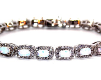 May include: A silver bracelet with a row of oval-shaped white opals set in a square frame with smaller clear stones around each opal.