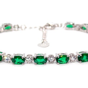 May include: A silver bracelet with emerald-green, rectangular gemstones and smaller, clear, round stones. The bracelet is displayed on a white background. The gemstones are set in a silver chain.