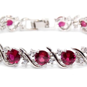 Könnte beinhalten: Ein silbernes Armband mit einem gedrehten Design verfügt über eine Reihe von roten Rubin-Steinen, die in der Mitte jeder Drehung eingesetzt sind. Das Armband ist mit kleineren klaren Steinen verziert.