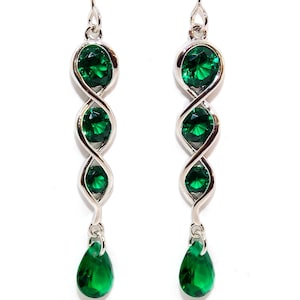 May include: Silver dangle earrings with a twisted design and three round green gemstones. The earrings have a teardrop-shaped green gemstone hanging from the bottom.