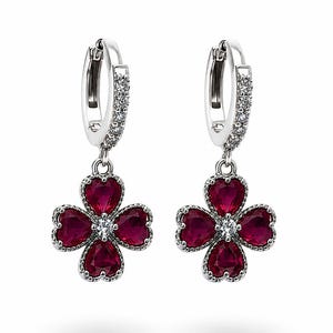May include: A pair of silver-toned hoop earrings featuring a dangling four-leaf clover charm. Each clover is composed of four deep red heart-shaped stones surrounding a central clear stone. The hoops are embellished with small clear stones.