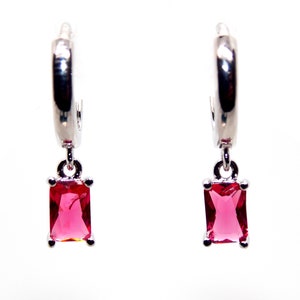May include: A pair of silver hoop earrings with a dangling square-shaped red gemstone.