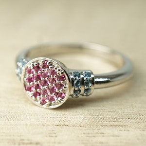 May include: A silver ring with a round pink gemstone surrounded by smaller blue gemstones.