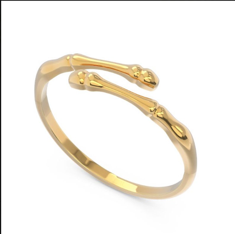K&ouml;nnte beinhalten: Ein goldfarbener Ring mit einem einzigartigen Design, das zwei ineinander verschlungene Knochen nachahmt. Der Ring ist offen und verstellbar.