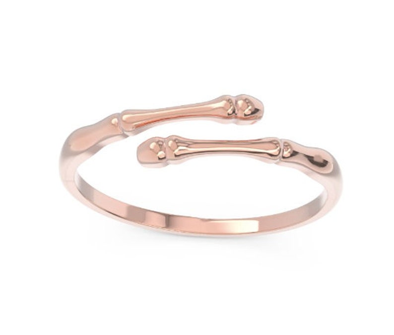 K&ouml;nnte beinhalten: Ein Ring aus Ros&eacute;gold mit einem einzigartigen Design, das zwei knochenf&ouml;rmige B&auml;nder zeigt, die sich um den Finger wickeln.