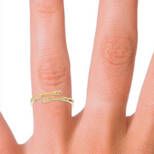 K&ouml;nnte beinhalten: Ein goldfarbener Ring mit einem einzigartigen Design, das zwei Knochen &auml;hnelt, die umeinander gewickelt sind. Der Ring wird an einem Finger getragen.