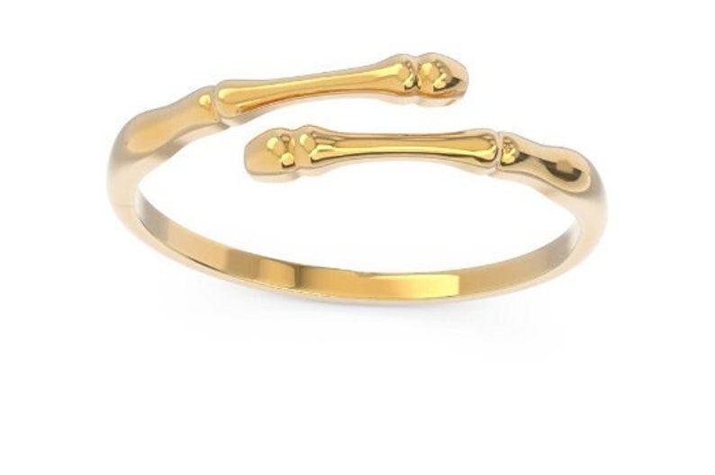 K&ouml;nnte beinhalten: Ein goldfarbener Ring mit einem einzigartigen Design, das zwei geschwungene, knochenartige Formen aufweist. Der Ring ist offen und verstellbar.