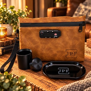May include: A tan faux leather pouch with a black zip, a black TSA007 combination lock, and a black wrist strap. The pouch features the letters JPF in a square frame. Included are a black cylindrical container with a lid and a black oval tray.