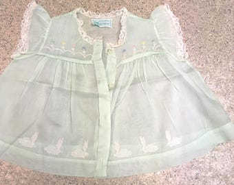 May include: A pale mint green sleeveless top featuring a button-down front, ruffled lace trim on the shoulders, and a lace-trimmed neckline. The garment includes embroidered floral details across the chest and white rabbit motifs along the hem.