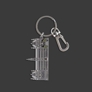 May include: Silver keychain featuring a detailed miniature replica of a building with a green roof. The keychain has a silver split ring and a silver lobster clasp.