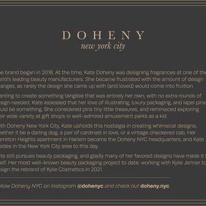 Op de afbeelding: Een donkergrijze afbeelding met de tekst "DOHENY new york city" in een schreefletter. De tekst beschrijft de oprichting van het merk in 2018, Kate Doheny's werk in beautyverpakkingen en haar samenwerking met Kylie Jenner.