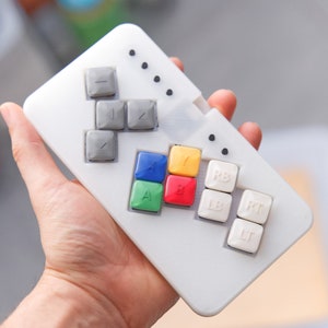 May include: A white plastic controller with grey and coloured buttons. The buttons are labelled A, B, X, Y, LB, RB, LT, and RT. The controller has a textured surface.