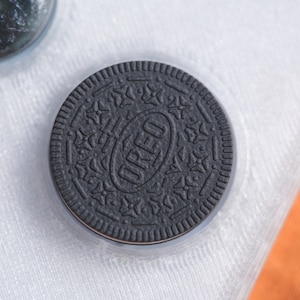 Puede incluir: Una galleta Oreo negra con la palabra "OREO" impresa en blanco en la parte superior.