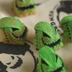 May include: Five green and black resin figurines of the character Jack Skellington from the movie The Nightmare Before Christmas. The figurines are all in different poses and have a textured surface.