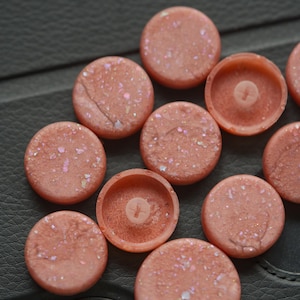 May include: A collection of ten round, pink, glittery, decorative buttons.