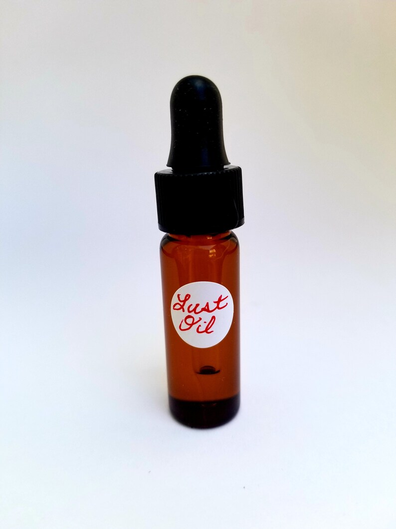 May include: A small brown glass bottle with a black dropper top. The bottle has a white label with the words "Lust Oil" written in red.