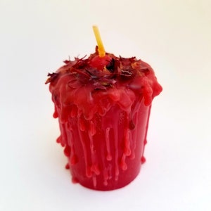 May include: A red candle with a wick and dried flower petals on top. The candle is dripping wax.