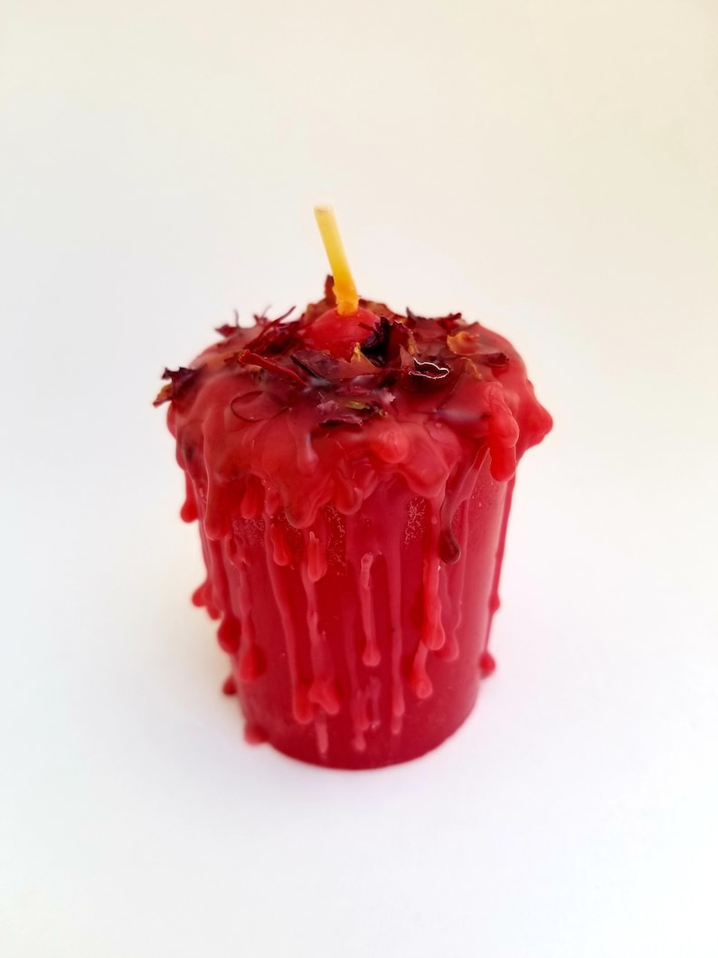 May include: A red candle with a wick and dried flower petals on top. The candle is dripping wax.