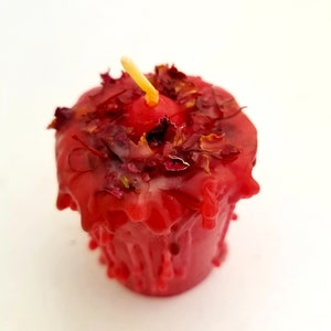 May include: A red candle with dried rose petals embedded in the wax. The candle is dripping wax and has a small wick.