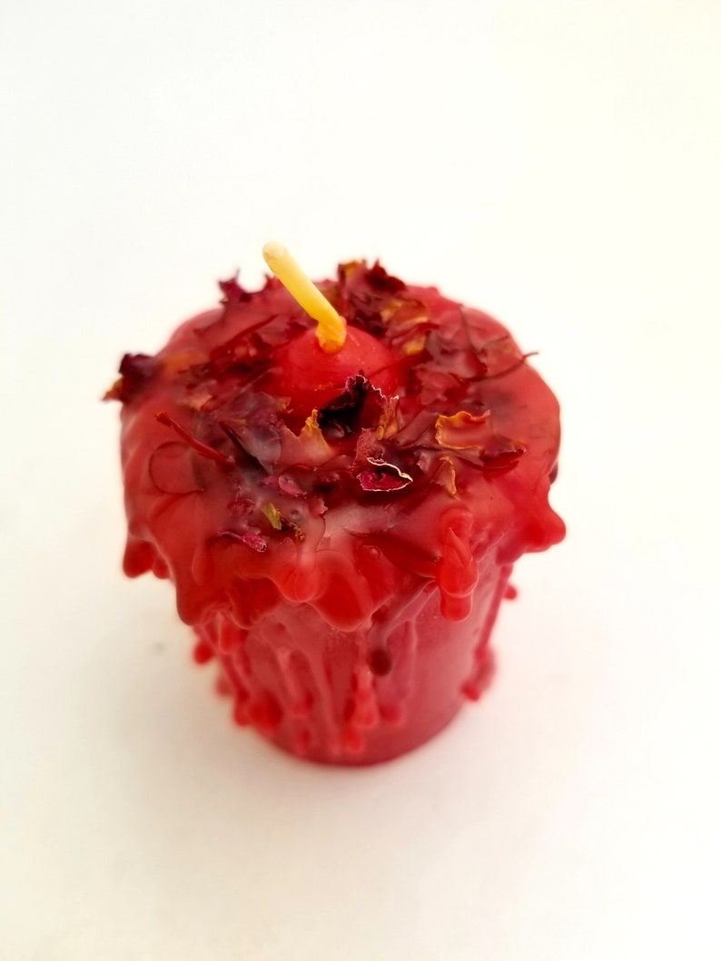 May include: A red candle with dried rose petals embedded in the wax. The candle is dripping wax and has a small wick.