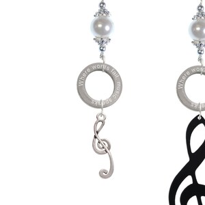 May include: Three silver keychains with a black leather bracelet. Each keychain features a silver charm with the words "Where words fail music speaks" and a pearl bead. The charms are attached to a silver treble clef, a black treble clef, and a silver heart with rhinestones.