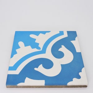 May include: A blue and white ceramic tile with a geometric pattern. The tile has a white background with a blue pattern of swirls and curves.