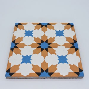 Può includere: Una piastrella quadrata in ceramica con un motivo geometrico. La piastrella presenta un disegno ripetitivo di stelle blu, arancioni, bianche e nere.