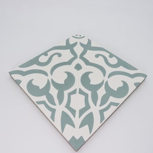 May include: A square ceramic tile with a white background and a blue patterned design. The pattern is a repeating design of stylized floral shapes.