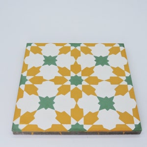May include: A square ceramic tile with a geometric pattern in shades of yellow, green, and white. The pattern features a repeating design of stars and diamonds.
