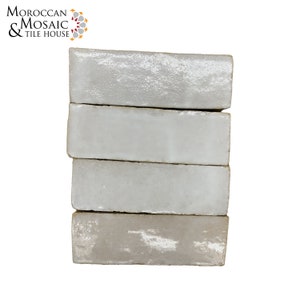 May include: Stack of four white glazed ceramic tiles. The tiles are rectangular and have a slightly textured surface.