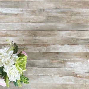 May include: A bouquet of white and pink flowers with green leaves against a light brown wood background.