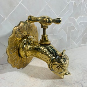 May include: A gold-toned brass faucet shaped like a bird's head with a decorative, ornate base. The faucet has a T-shaped handle.