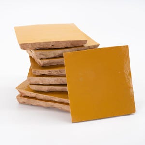 May include: A stack of yellow ceramic tiles with a single tile laying flat in front of the stack.