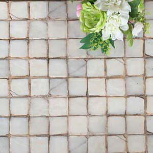 May include: White and green floral arrangement with pink accents on a white tiled background.