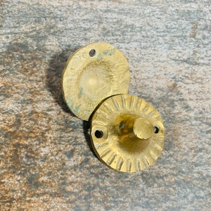 May include: Two gold-toned metal door knobs with a decorative design. The top knob has a smooth surface and the bottom knob has a textured surface.