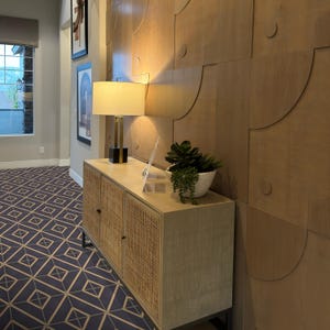 May include: A wooden cabinet with a woven rattan front, a lamp with a white shade, and a potted plant on top. The cabinet is in a hallway with a patterned floor.