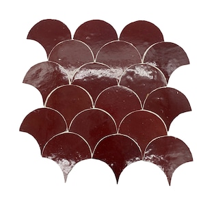Puede incluir: Una hoja de azulejos de cerámica de color rojo burdeos en forma de escamas de pez. Los azulejos son brillantes y tienen un mortero blanco.