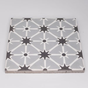May include: A gray ceramic tile with a repeating pattern of black stars and white circles. The tile has a slightly textured surface.